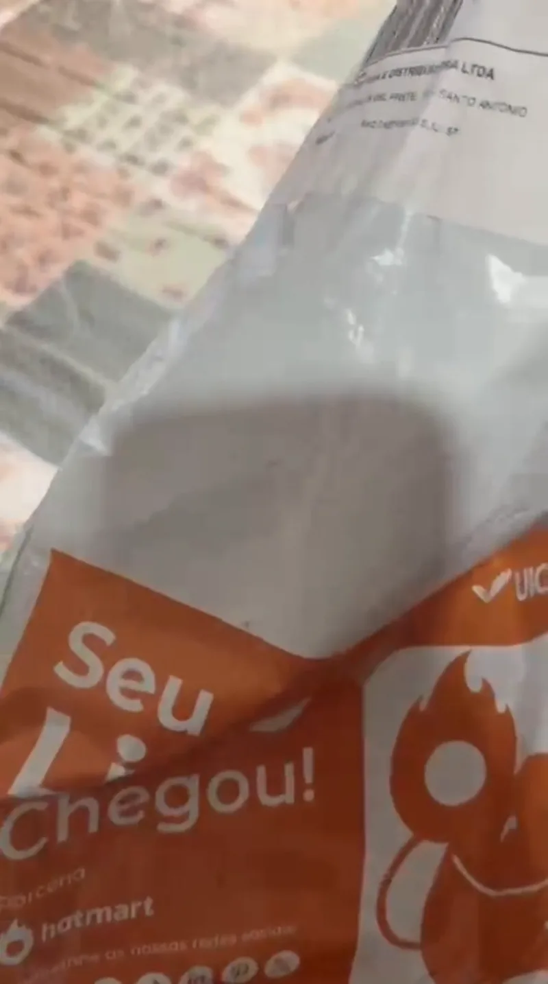 Envelope laranja e branco da UICLAP com a frase Seu livro chegou, sobre uma colcha.